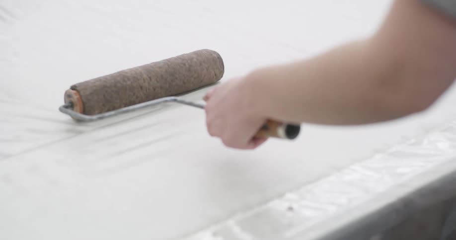 Woman moves a paint roller across a sheet lying on a plastic covered table