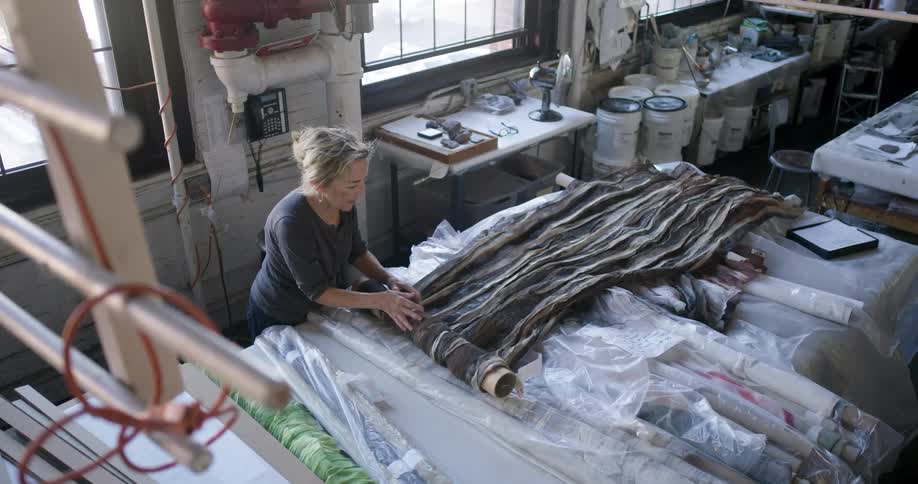 Woman rolls fabric onto a cardboard tube while working in a workshop during the daytime