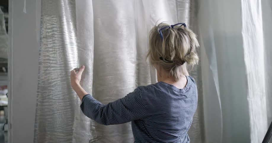 Woman examines and adjusts a large translucent fabric with a metallic texture