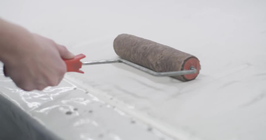 A person uses a paint roller to smooth out a plasticcovered surface with a second roller positioned nearby rolling in the opposite direction creating a sense of mirrored motion