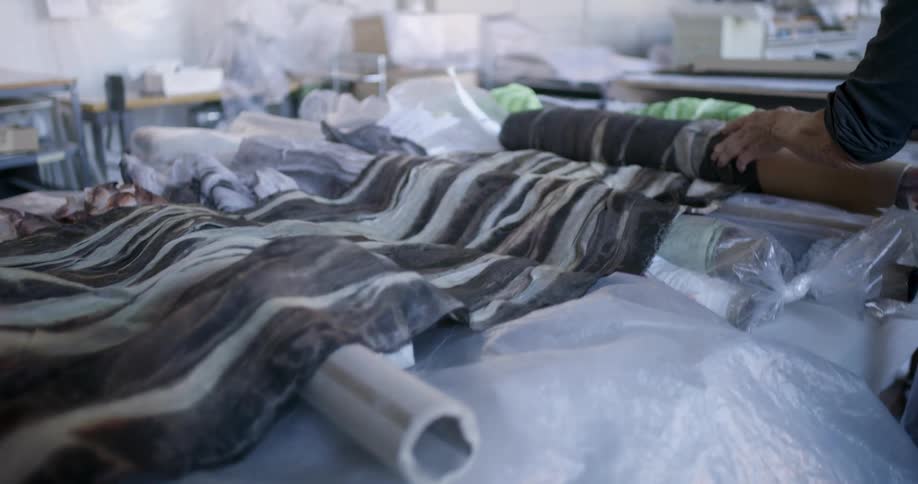 Person unrolls a patterned fabric with a wavy texture over a plasticcovered surface