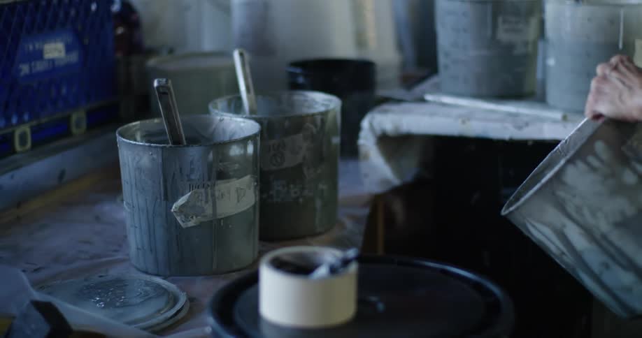 A woman points to a paint bucket while talking to another woman in a paint studio