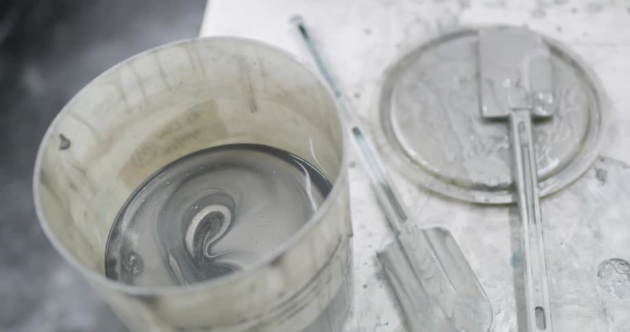 Silver paint is in a bucket and on a spatula on a lid