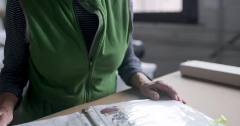 A woman wearing eyeglasses and a green vest is studying a sample catalogue