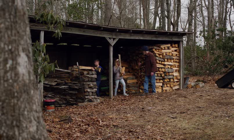 An adult man next to two children who are picking up pieces of wood at an outdoor lumber yard