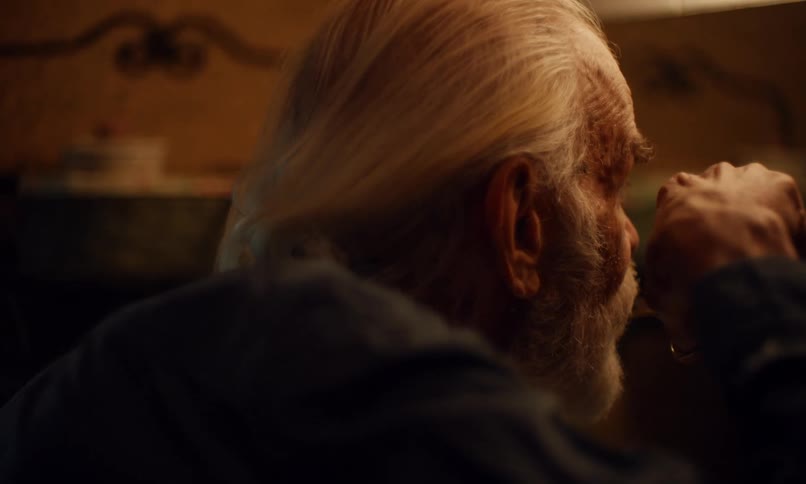 Elderly white haired man trims his mustache with a pair of scissors
