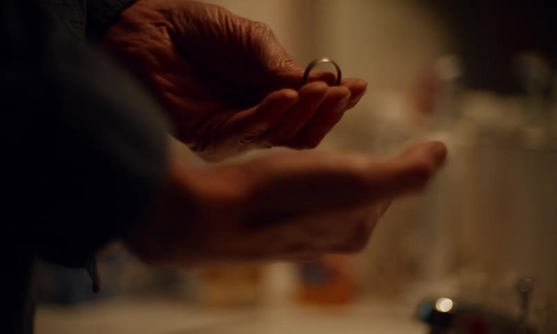 Elderly person examines a wedding ring then closes a hand tightly over it