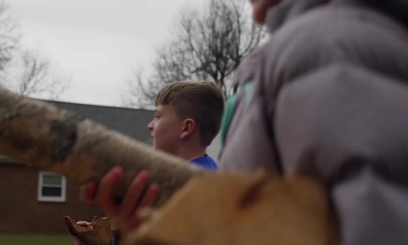 Siblings walk past houses in winter carrying pieces of wood