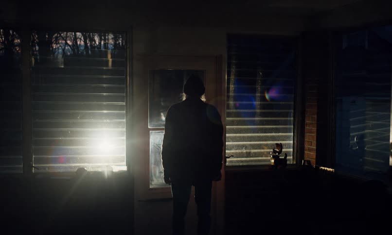 Arriving vehicle casts a man standing near the door of his house into silhouette at night