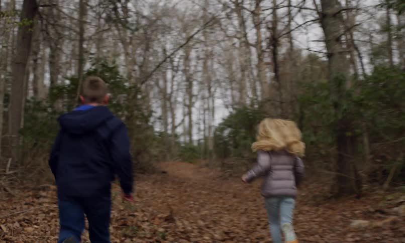 Two children running through the dry leaves of a forest