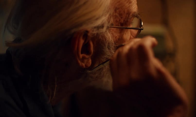 Side portrait of an elderly man cutting his white beard with small scissors