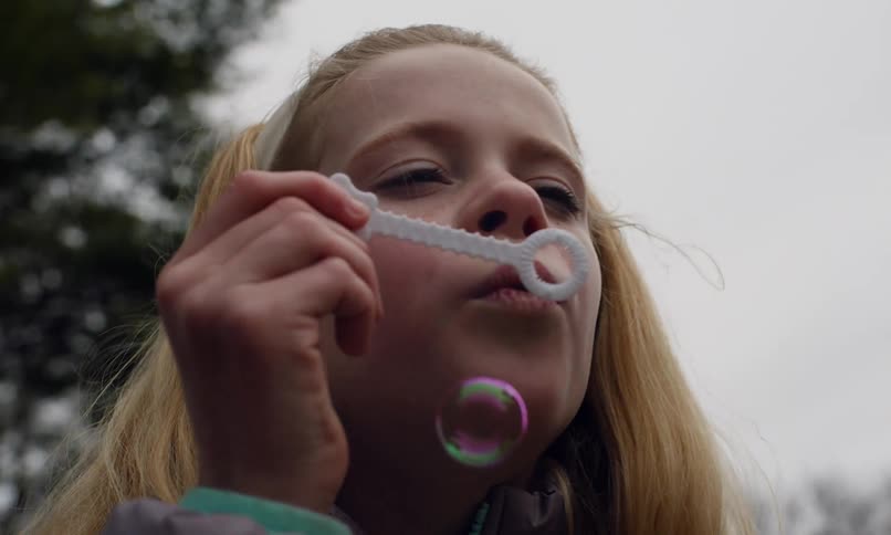 Two children accompanied by their grandfather playing with soap bubbles outdoors on a cloudy day