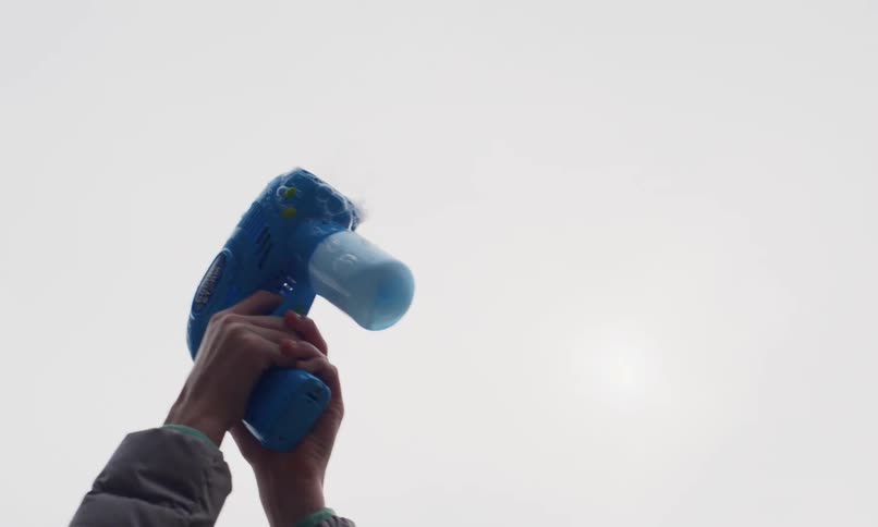 A girl in a puffy jacket plays with a blue bubble gun