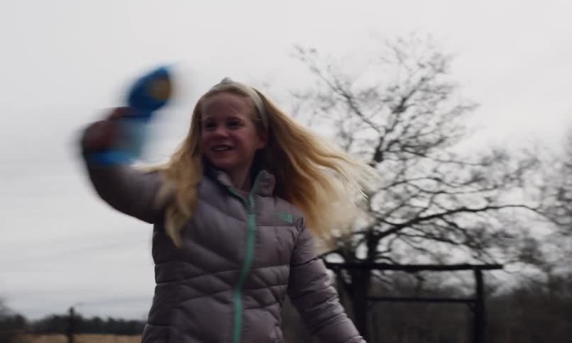 Blonde girl in a backyard on a cloudy day playing with a bubble gun