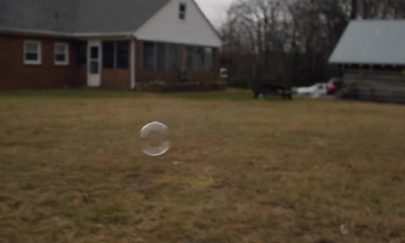 Bubbles float across a yard in front of a brick house and a shed