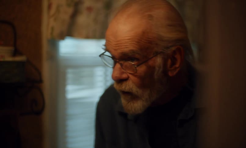 Reflection of an elderly man in the bathroom mirror cutting and combing his beard