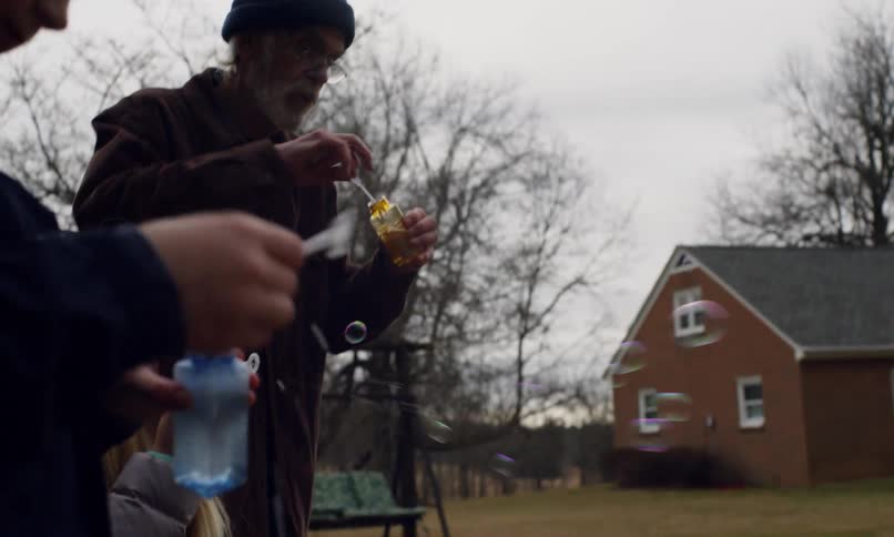 Grandfather and his grandchildren stand in the yard of a rural home and bubbles