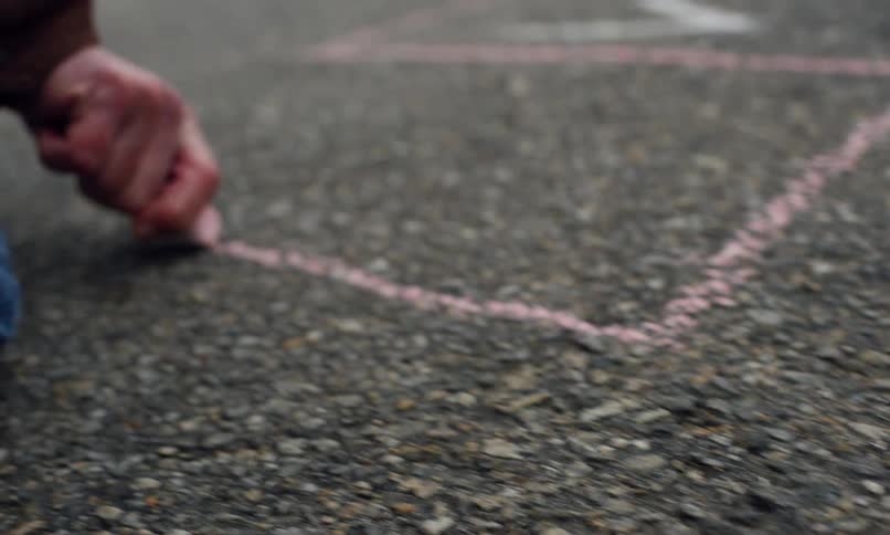 Man kneeling on asphalt near a parked car in a residential neighborhood draws with chalk