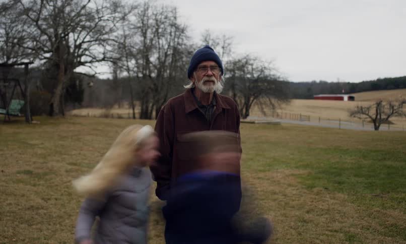 Children run around their grandfather in a fenced field on a winter day