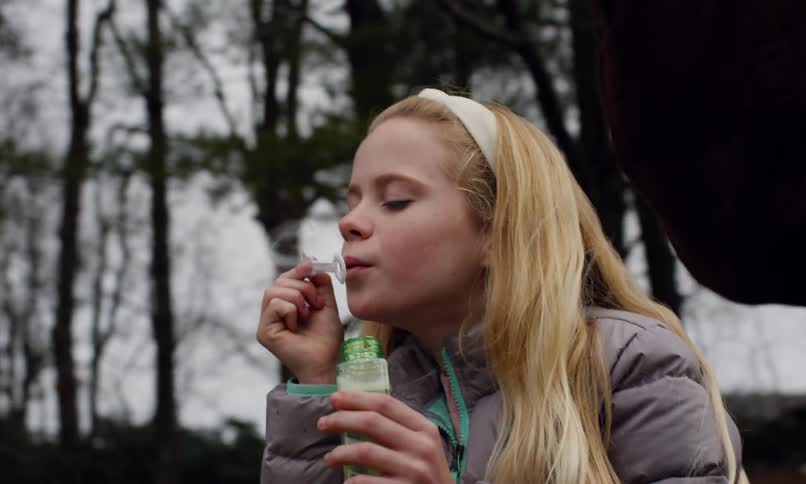 Girl smiles while she and her brother bubbles in a field near a grove of trees with their grandfather