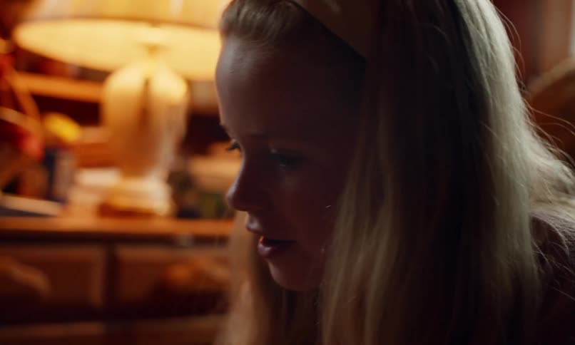 A young girl with long blonde hair and braces is laughing joyfully her face illuminated by warm indoor lighting with a cozy living room setting in the background