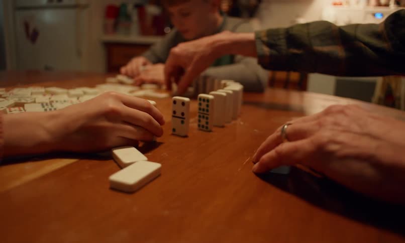 Three peoples hands arrange dominoes in a circle on a wooden table