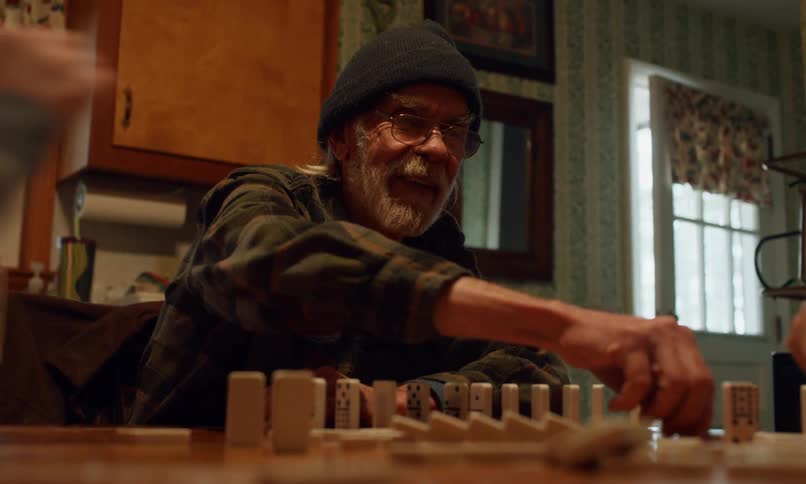 A young girl and an older man are playing dominoes at a table in a cozy patterned wallpapered room