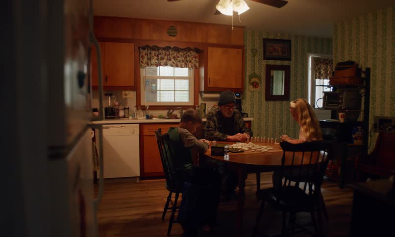 Family sitting around a wooden table in a cozy kitchen playing a board game under soft light