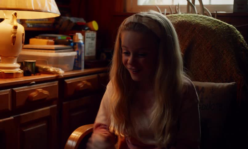 A blonde girl with long hair sits on a chair in a cozy room having fun and celebrating with her little brother