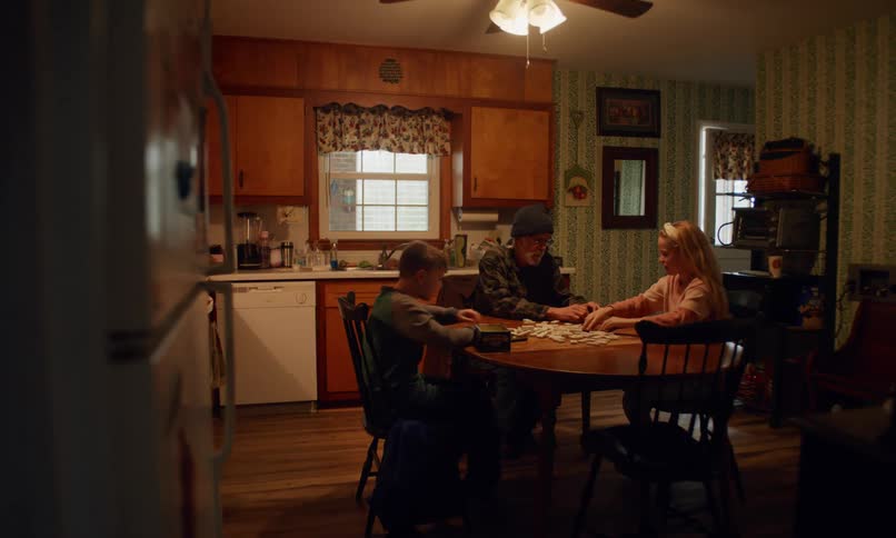 A family sits at a table in the ktchen and plays with dominoes