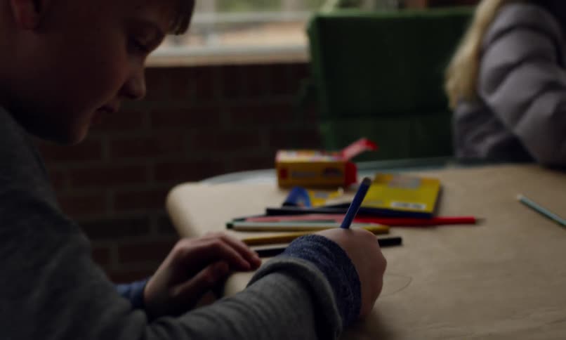 A girl and a boy are sitting at a table coloring with colored pencils and crayons
