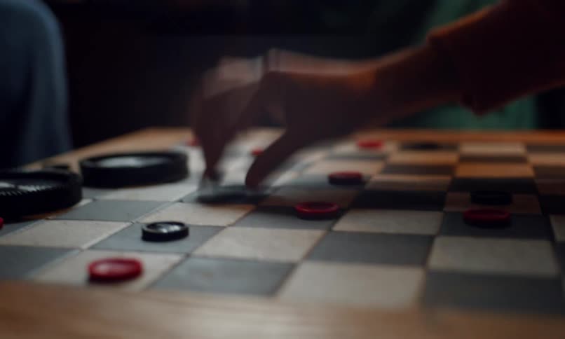 Players move pieces on a wooden checkerboard during a game
