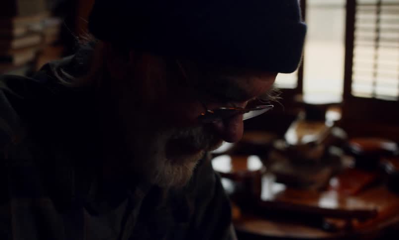 Portrait of an elderly man wearing glasses sitting in a living room talking and playing a board game with two other people