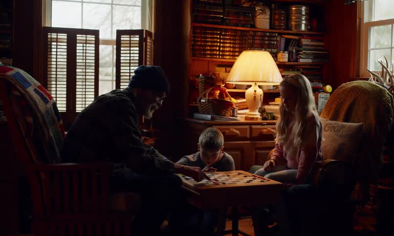 An elderly man is playing checkers with his grandkids in a cozy room at home