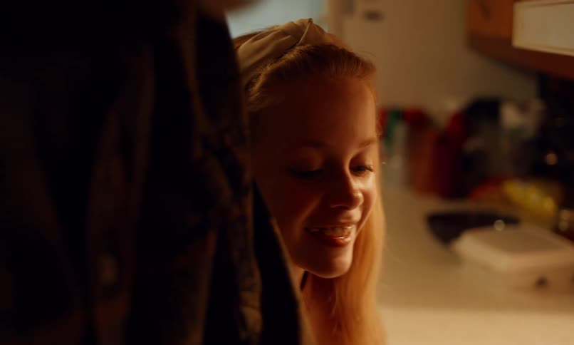 A girl in a kitchen smiles as she looks up at an adult