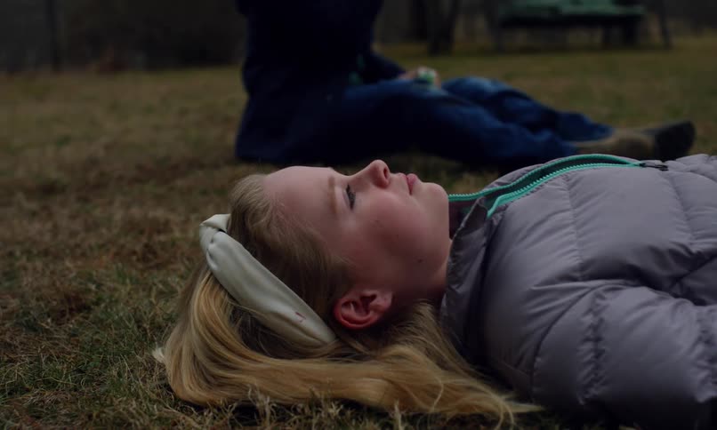 A boy plays with bubbles as his sister lays on the grass staring at the sky