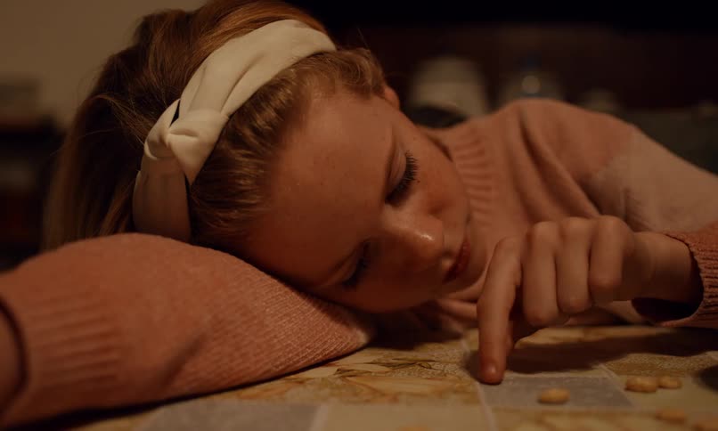 A girl lays her head on the table as she plays with cereal with one hand