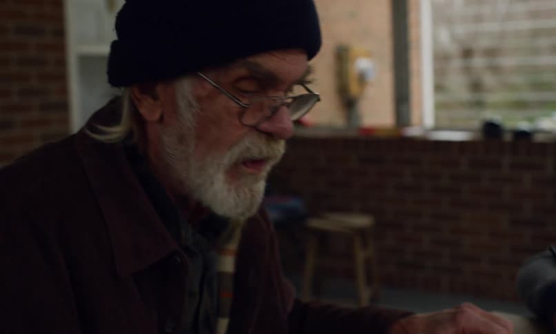 An elderly man is talking as he looks around a room