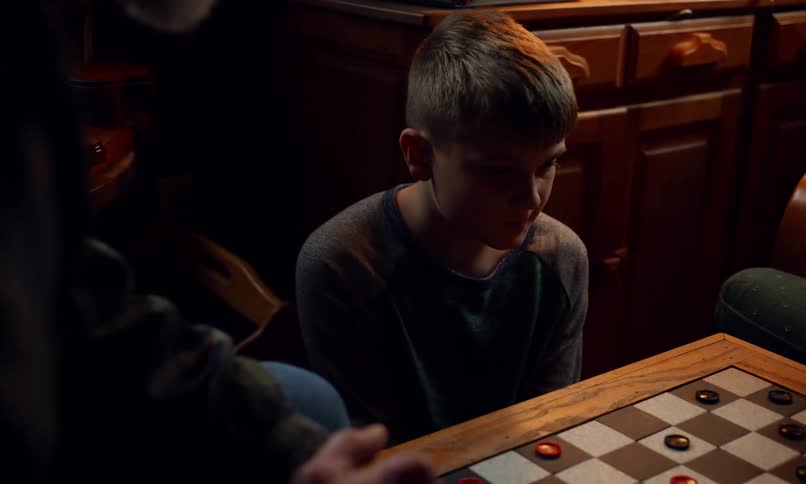 Two children and an adult are playing checkers at a table in a dimly lit room