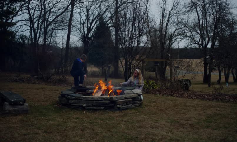 A brother and sister are staring at a bonfire in a stone firering