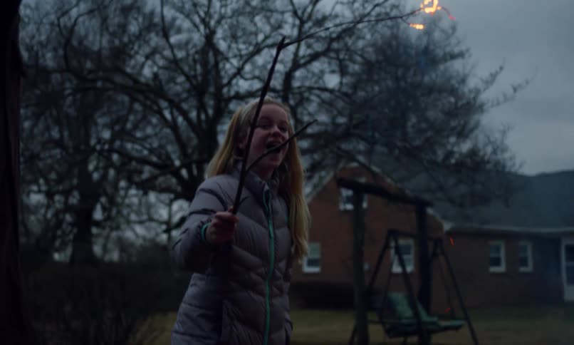 Little blonde girl in a backyard having fun while burning a twig in a bonfire