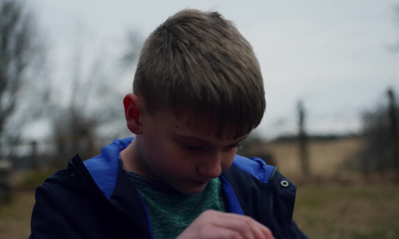 A young boy plays with bottled bubbles in a grassland on a cloudy winter day