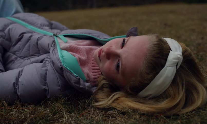Happy little blonde girl lying on grass outdoors
