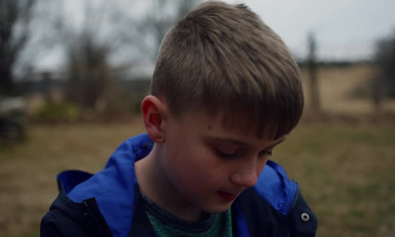 A boy is standing outside and blowing bubbles with a wand