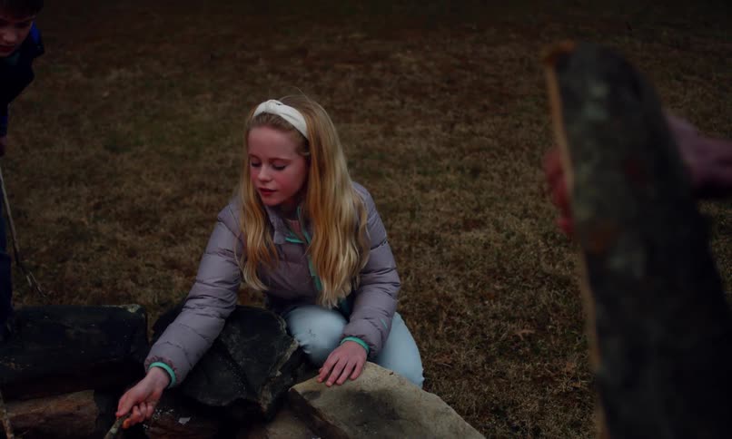 Two kids use sticks to poke at a fire in a stone ring