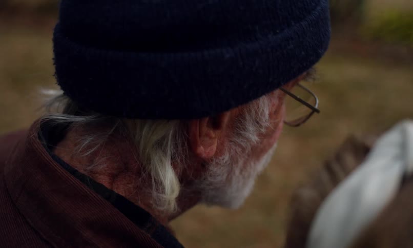 Side portrait of an elderly man sitting outdoors with a person next to him