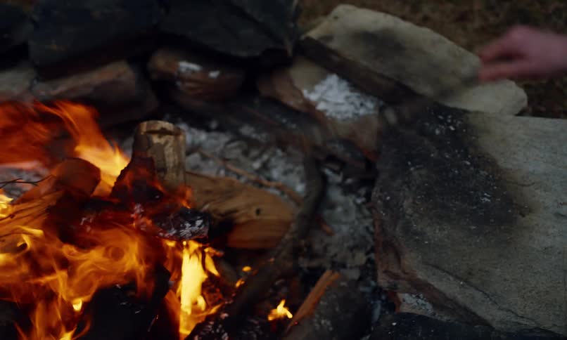 A boy and girl are using sticks to poke at a fire in a stone ring