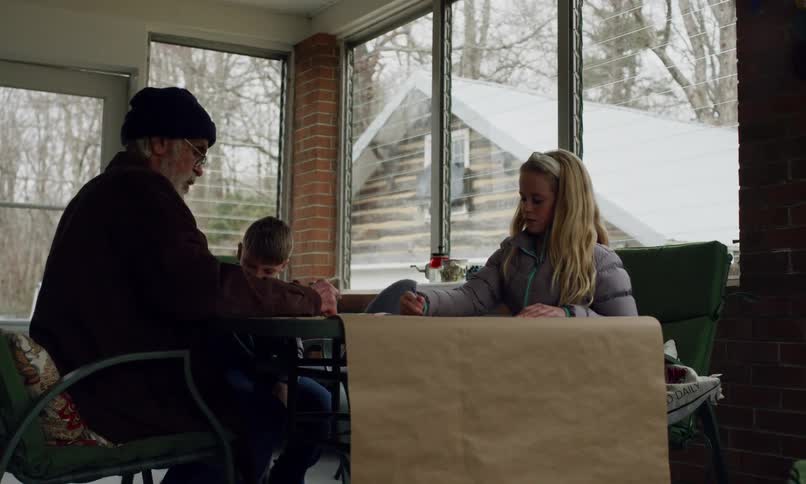 A man and two children are indoors coloring on a snowy day