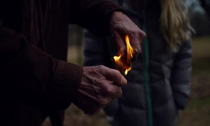 Pair of hands of a person lighting a lighter and burning dry leaves next to a little girl