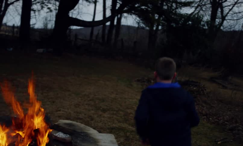 An elderly man plays with his grandkids around a campfire in the countryside